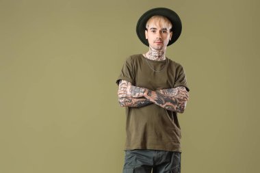 Young tattooed man in hat on green background