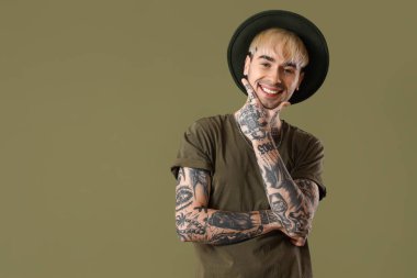 Young tattooed man in hat on green background