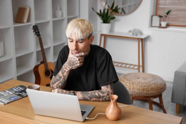 Young tattooed man using laptop at home