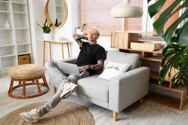 Young tattooed man using laptop on sofa at home