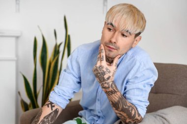 Young tattooed man sitting in armchair at home