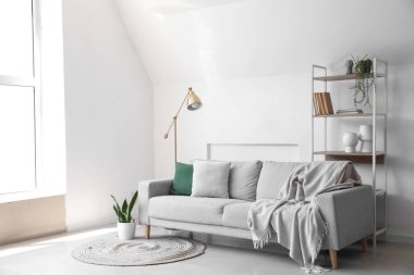 Interior of light living room with shelving unit, sofa and lamp