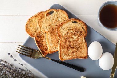 Plate with toasts, eggs and cup of tea on light wooden background, closeup