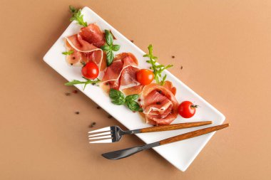 Plate with slices of delicious jamon and tomatoes on color background