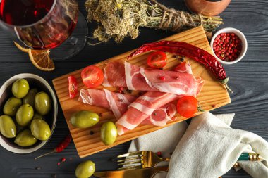 Composition with delicious jamon, olives and spices on dark wooden background