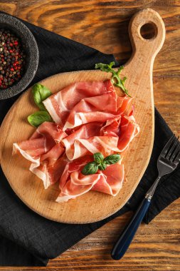 Board with slices of delicious jamon on wooden background
