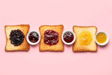 Delicious toasts and bowls of jam on pink background