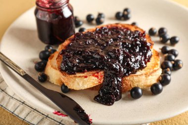 Plate with tasty toast and black currant on beige background, closeup
