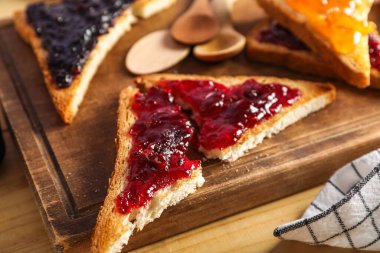 Board with tasty toast and raspberry jam on beige background, closeup
