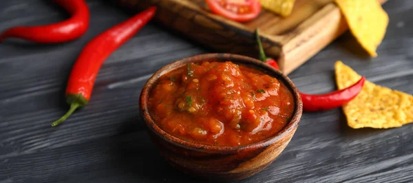Bowl of tasty salsa sauce on black wooden background