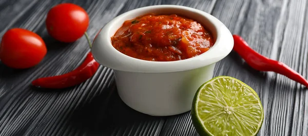 Bowl of tasty salsa sauce on dark wooden table