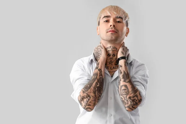Young tattooed man in white shirt on light background