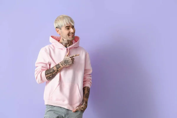 Young Tattooed Man Pink Hoodie Pointing Something Lilac Background —  Fotos de Stock