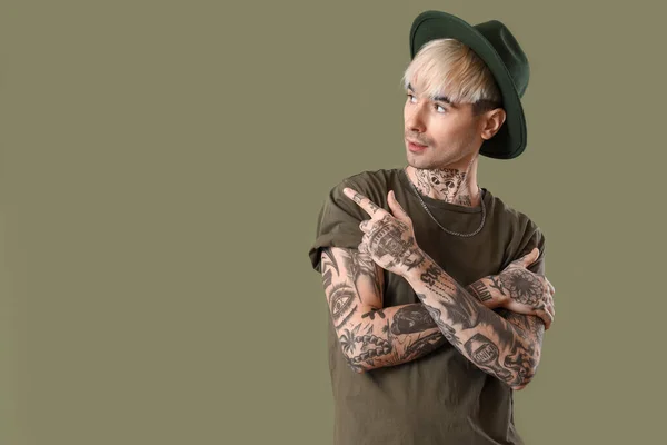 Young tattooed man in hat pointing at something on green background