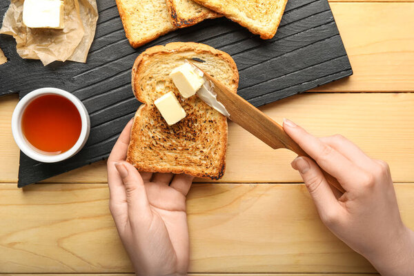 Woman spreading butter onto toast on wooden background