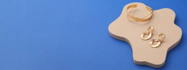 Stylish golden bracelet and earrings on blue background with space for text