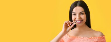 Beautiful young woman with sweet chocolate candy on yellow background with space for text