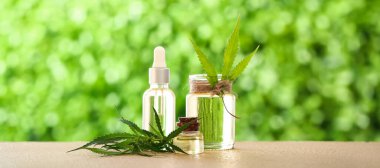 Bottles of healthy hemp oil and leaves on table outdoors