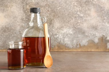Bottles of maple syrup and spoon on grunge background