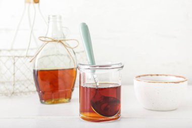 Glass jar of maple syrup and spoon on light background