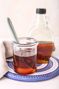 Board with glass jar and bottle of maple syrup on light background, closeup