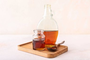 Wooden board with bottles of maple syrup on light background