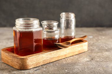 Wooden board with jars of tasty maple syrup on table