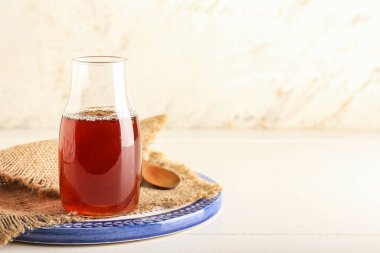 Board with bottle of maple syrup on light background