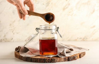 Woman pouring maple syrup from spoon into jar on table