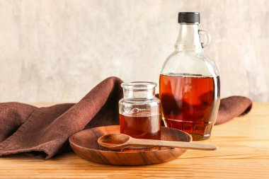 Plate with bottle and spoon with maple syrup on wooden table