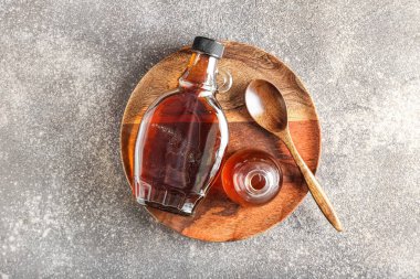 Wooden plate with bottles of maple syrup and spoon on grunge background