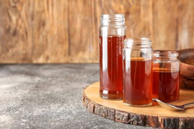Wooden board with jars of maple syrup on table