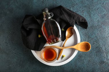 Tray with bottle and bowl of tasty maple syrup on dark color background
