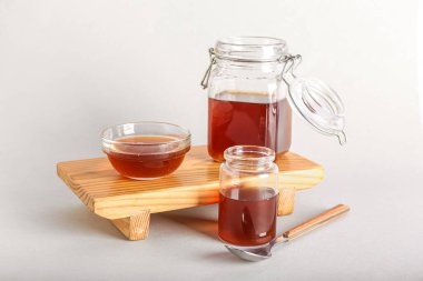 Wooden board with jars and bowl of tasty maple syrup on white background