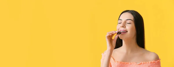 Beautiful Young Woman Eating Sweet Chocolate Candy Yellow Background Space — Fotografia de Stock