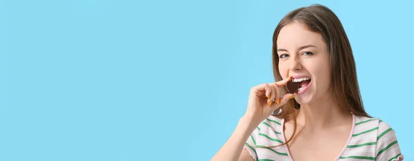 Beautiful Young Woman Eating Chocolate Candy Blue Background Space Text — Stockfoto