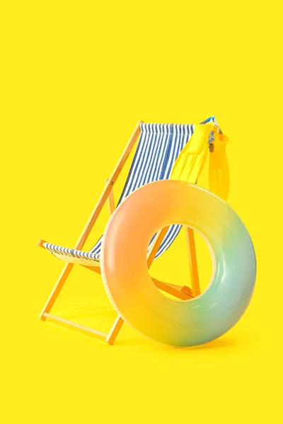 Wooden deck chair with inflatable ring and paddles on yellow background