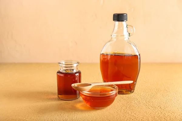 Bottles and bowl of maple syrup on color background