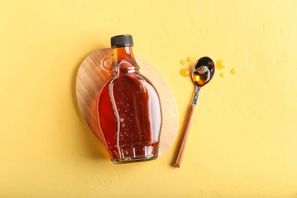Bottle and spoon of maple syrup on color background