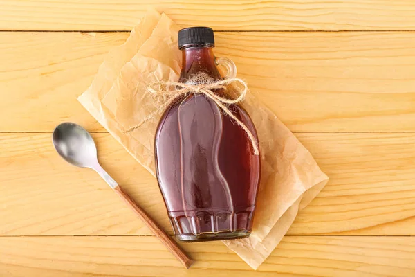 Bottle of maple syrup and spoon on wooden background