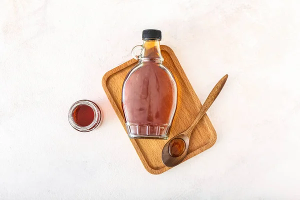 Composition with bottles and spoon of maple syrup on light background