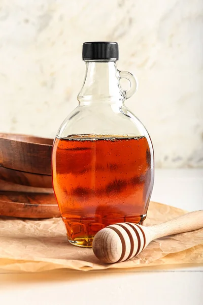Bottle of tasty maple syrup and honey dipper on light wooden background