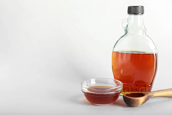 Bottle, bowl and spoon of maple syrup on white background