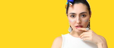 Fashionable woman with glitters on face against yellow background with space for text