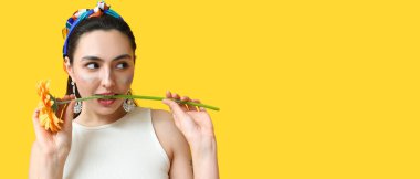 Fashionable woman with glitters on face holding flower against yellow background with space for text