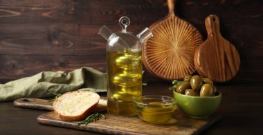Composition with bottle of fresh oil, bread and olives on wooden background