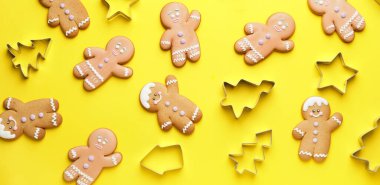 Tasty gingermen and cookie cutters on yellow background, top view