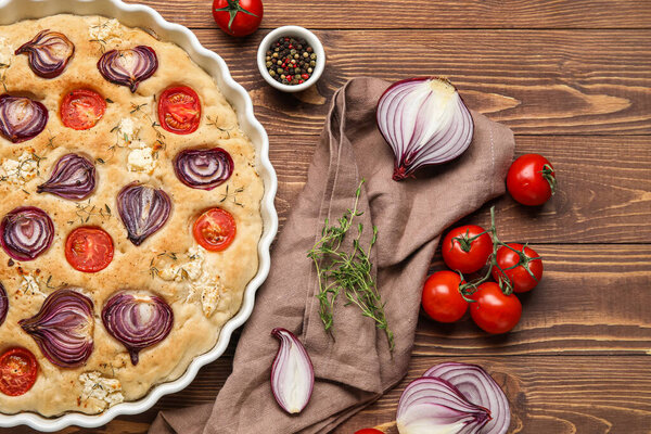 Baking dish with tasty Italian focaccia and vegetables on wooden background
