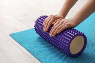 Woman training with foam roller on blue fitness mat at home, closeup