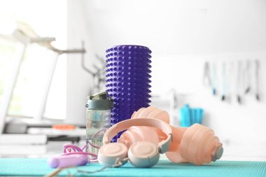 Foam roller with headphones, dumbbells, bottle and skipping rope on mat in gym